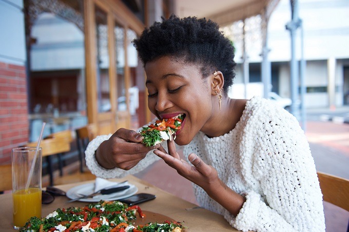 Young, black woman eating a vegetarian pizza