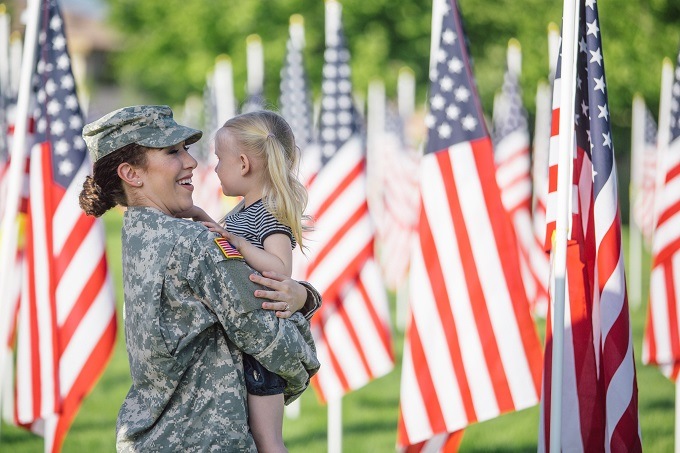 military woman holding a young girl in the middle of many American flags outside