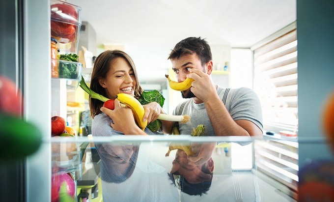 White young adult female and male smiling and holding bananas and other fruit and produce