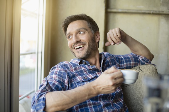 smiling man looking out the window with coffee