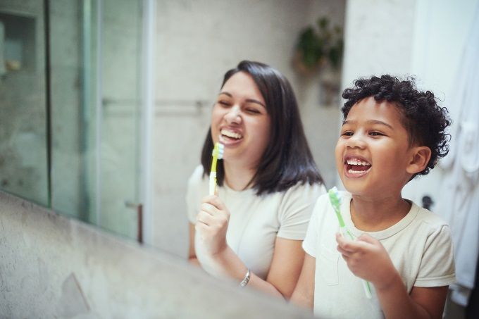 Mixed mom and toddler child laughing and brushing their teeth