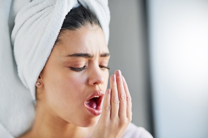 woman with wet hair in a towel checking the freshness of her breath