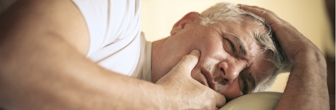 Man laying down holding his mouth due to mouth pain