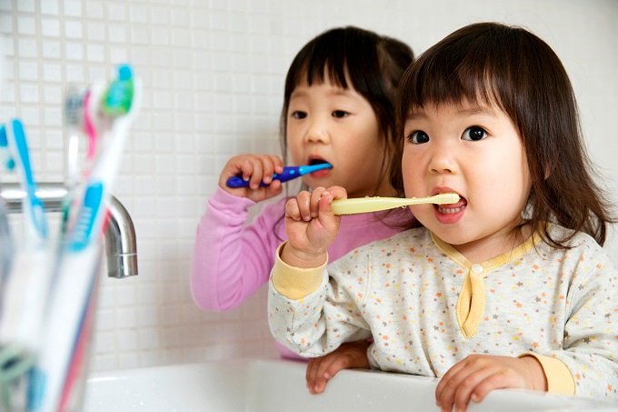 Two toddler Asian children brushing their teeth by bathroom sink