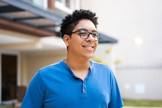 young mixed male in blue shirt with glasses smiling