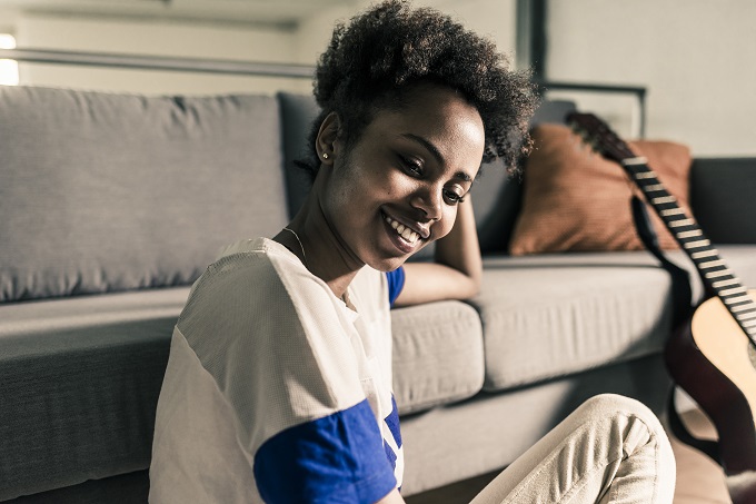 Young African American woman inside by a couch, relaxing and smiling