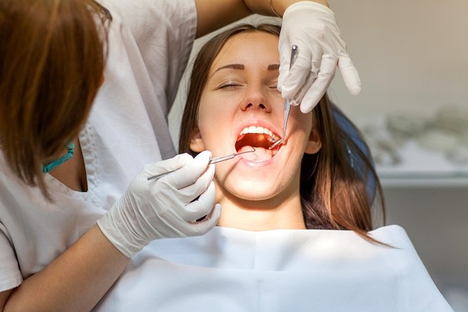 White young female adult in dental chair with white female dentist checking teeth
