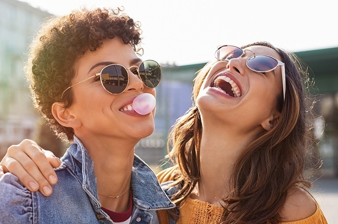 mixed young women laughing outside and one is blowing a bubble with her gum