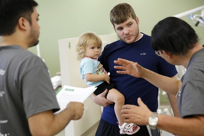 mixed people with dad holding toddler daughter talking to two dental professionals