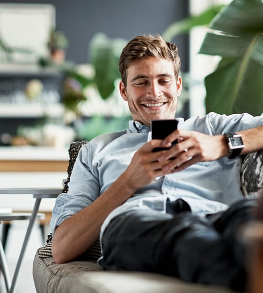 smiling man laying on couch looking at his phone