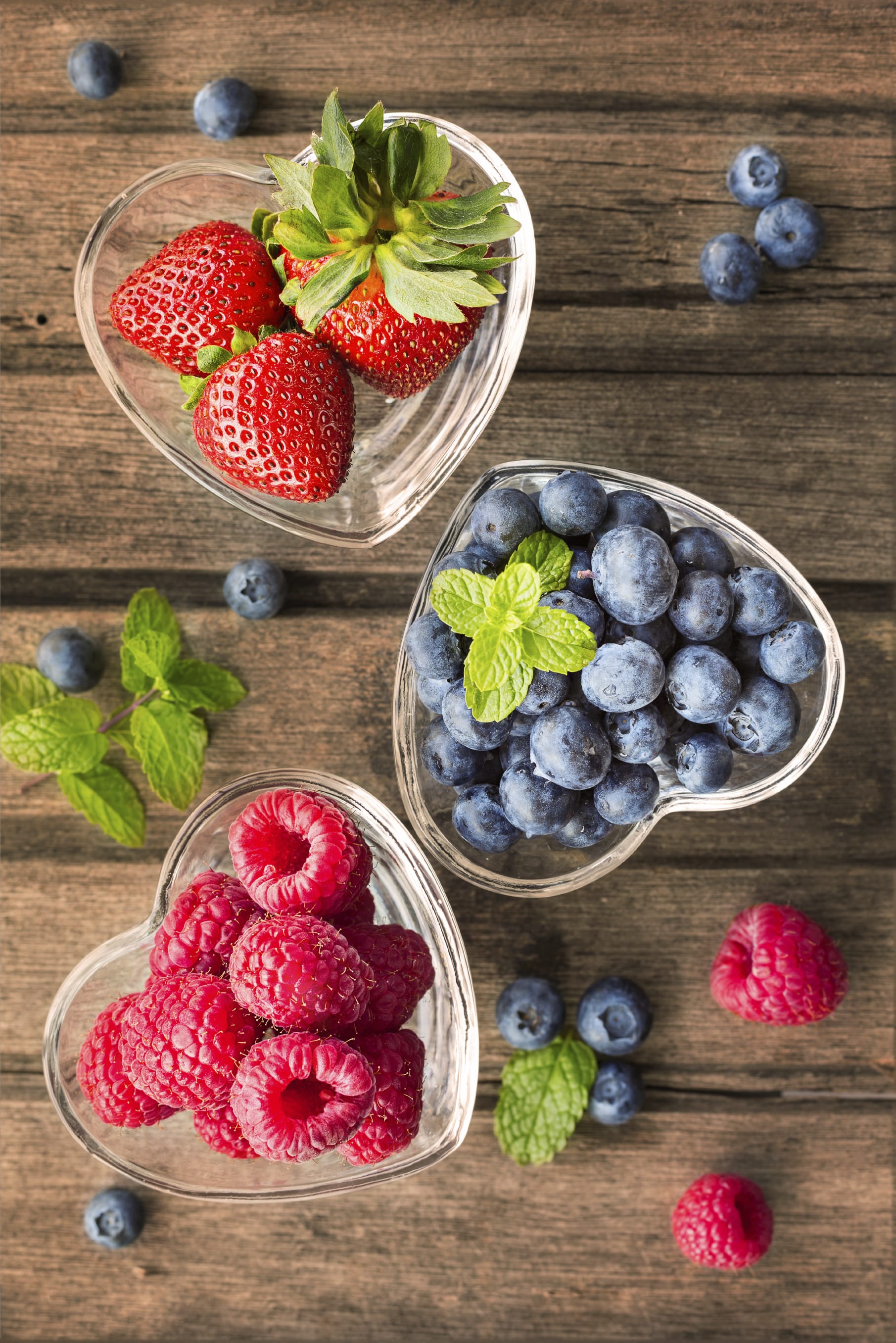 Mix of fresh berries in a glass ramekins in shape of heart, on w